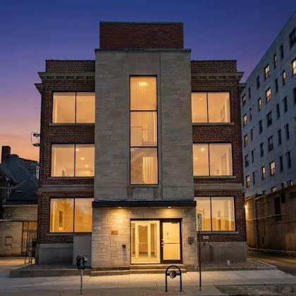 a building with a brick facade stands in the middle of a street at dusk.