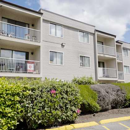 apartment building with balconies and bushes in front.