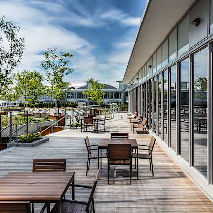 a wooden deck with tables and chairs is surrounded by glass walls.
