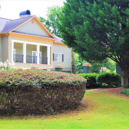 a house with a grey roof and a yellow trim is surrounded by a green lawn and a hedge at woodside village apartments, clarkston, ga 30021