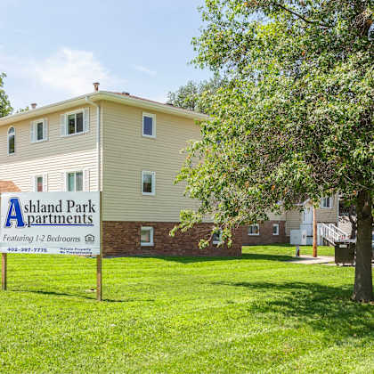 a sign for ashland park apartments is in front of a two-story building.