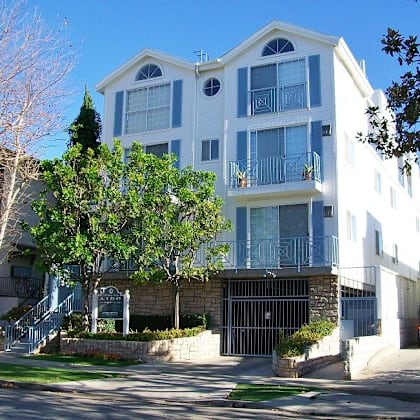 a white and blue two story apartment building with a black gate in front.
