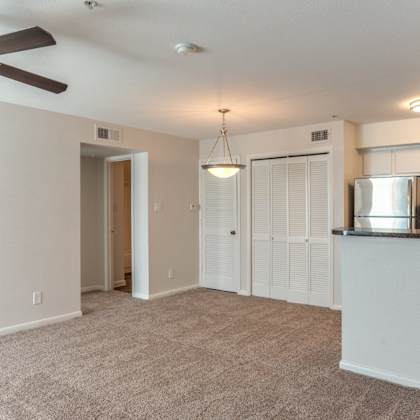 a spacious living room with a ceiling fan and a kitchen area with a refrigerator.