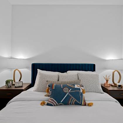 a bed with a blue headboard and a white comforter with a pillow and a teddy bear on it.