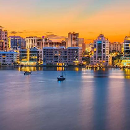 a city skyline at dusk with buildings reflecting on the water.