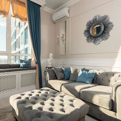 a living room with a grey couch and a round mirror on the wall.