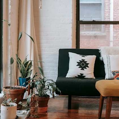 a living room with a black couch, a wooden table, and several potted plants.
