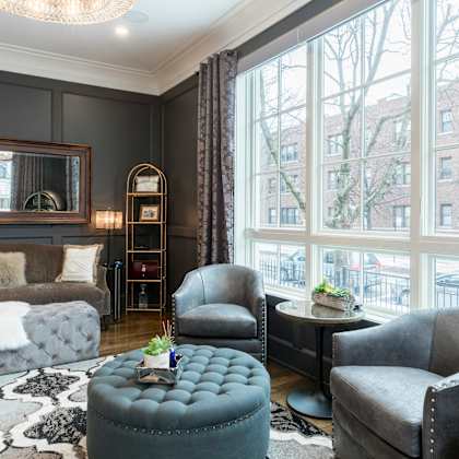 a living room with a grey couch, a grey armchair, a grey ottoman, and a black and white rug.