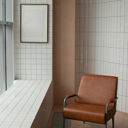 a brown leather chair sits in front of a wall with white tiles.