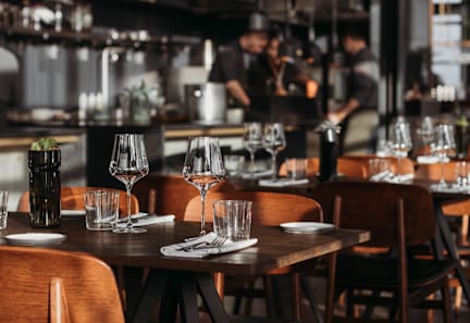 A restaurant with wooden tables and chairs and glasses on the tables.