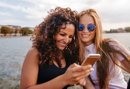 Two women are looking at a smartphone together by the water.