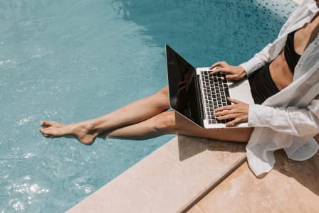 a woman sitting on the side of a pool working on her laptop