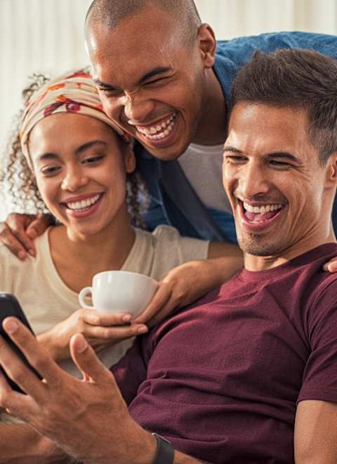 A group of friends are gathered around a man who is holding a smartphone.