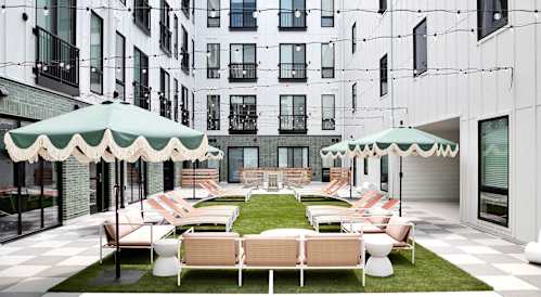 A patio with white furniture and green umbrellas is surrounded by white buildings.