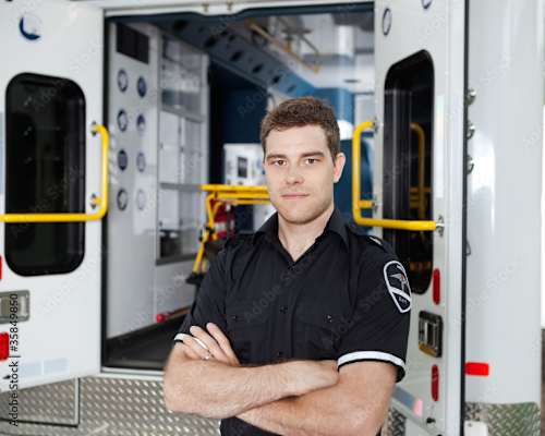A man in a black shirt is standing with his arms crossed in front of an ambulance