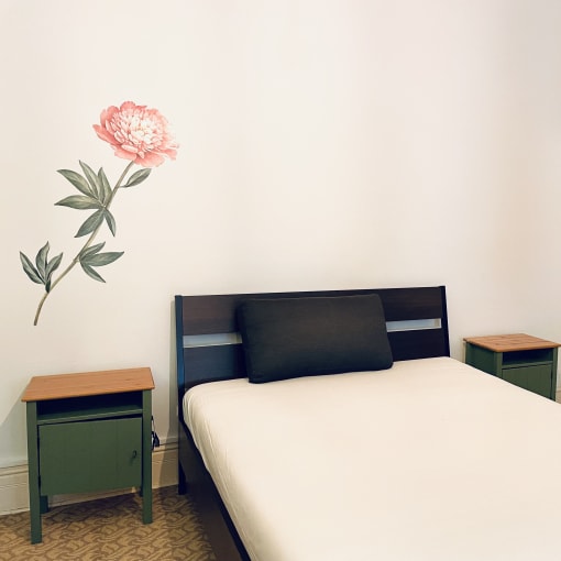 a small bedroom with a bed and a pink flower on the wall