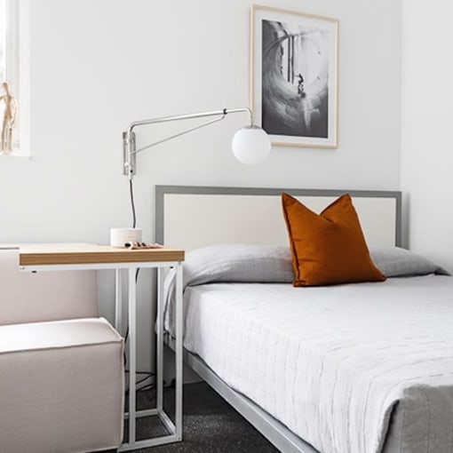 a white bedroom with a bed and a orange pillow