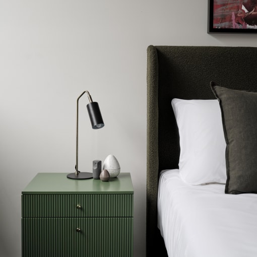 a bedroom with a bed and a green nightstand with a lamp on it