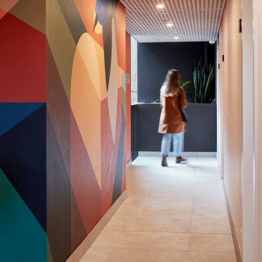 a woman walking down a hallway with a colorful wall mural