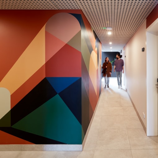 a hallway with a colorful wall mural and people walking down it