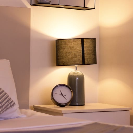 a nightstand with a clock and a lamp and a shelf with books