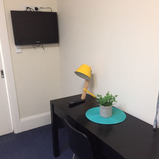 a small desk with a lamp and a tv on the wall