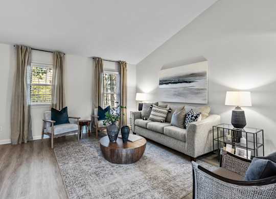 A living room with a grey couch, a coffee table, and a large painting on the wall at West Oak Apartments, Wake Forest