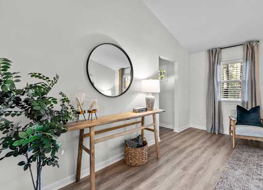 A room with a round mirror, a wooden table, a chair, and a potted plant at West Oak Apartments, Wake Forest, 27587