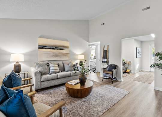A living room with a grey couch, a wooden coffee table, and a large painting on the wall at West Oak Apartments, Wake Forest, NC 27587