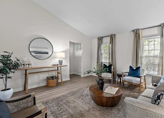 A living room with a grey couch, a wooden coffee table, and a mirror on the wall at West Oak Apartments, North Carolina