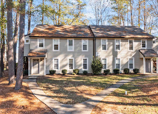 A large house with a grey roof and white walls is surrounded by trees at West Oak Apartments, Wake Forest, 27587