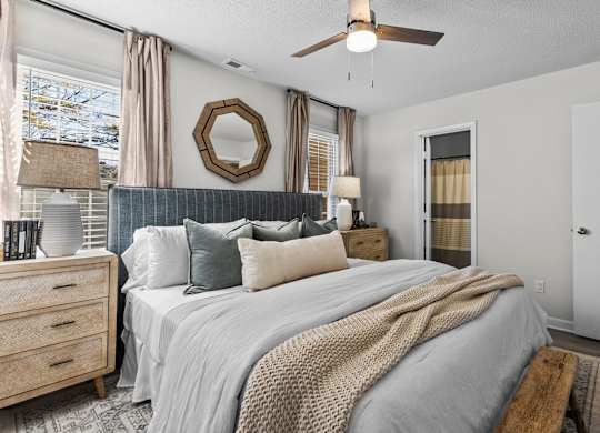 A bedroom with a large bed, a ceiling fan, and a mirror on the wall at West Oak Apartments, Wake Forest, NC 27587