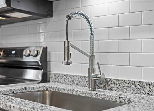 A kitchen sink with a chrome faucet and a tile backsplash at West Oak Apartments, Wake Forest, 27587