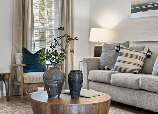 A living room with a grey couch, a wooden table, and a painting on the wall at West Oak Apartments, North Carolina