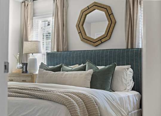 A bedroom with a bed, pillows, a mirror, and a lamp at West Oak Apartments, North Carolina 27587