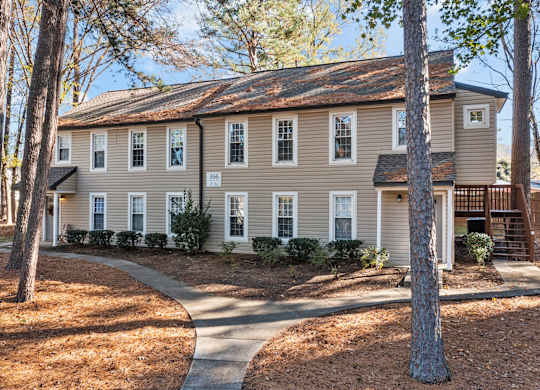 A two-story house with a driveway and trees in front at West Oak Apartments, Wake Forest, NC 27587