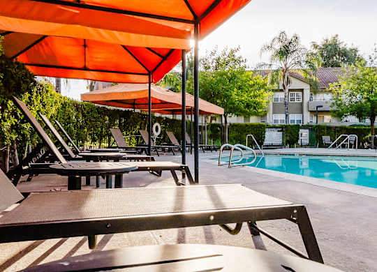 A poolside area with sun loungers and an orange umbrella. at Legends at Rancho Belago, Moreno Valley