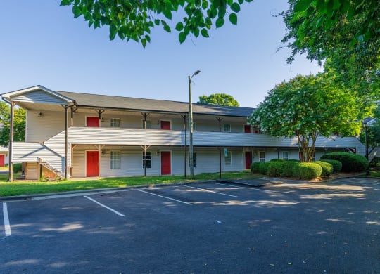 an empty parking lot in front of a white building with red doors at Ashford Place Apartments, Kannapolis, NC