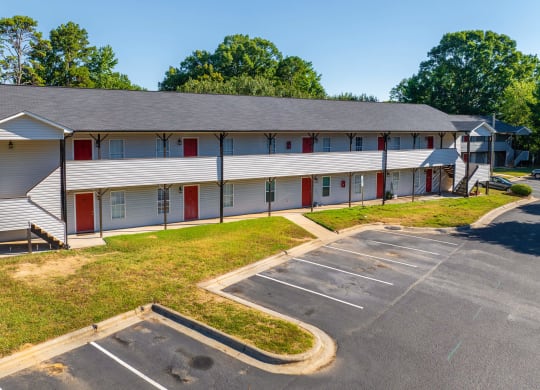 a white building with red doors and a parking lot at Ashford Place Apartments, Kannapolis 