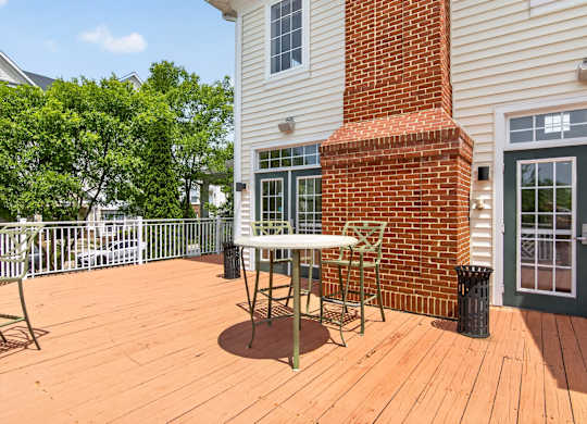 A wooden deck with a table and chairs is in front of a house.