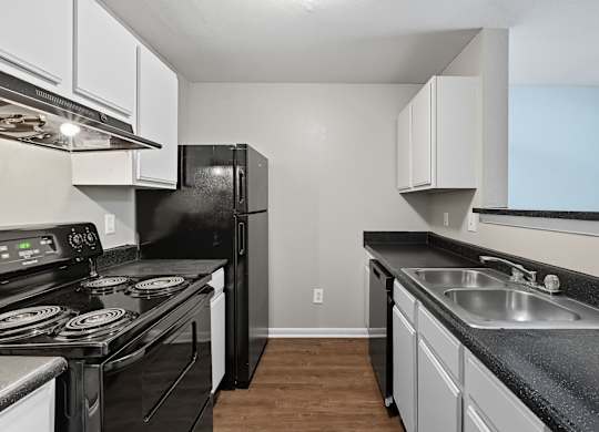 A black refrigerator sits in a kitchen with white cabinets. at Greens at Stonecreek, Lithonia, GA, 30038