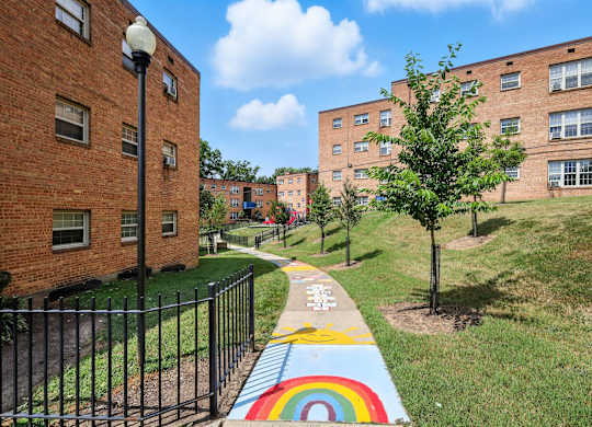 A rainbow painted on a sidewalk in front of a black fence at Huntwood Courts Apartments, Washington DC