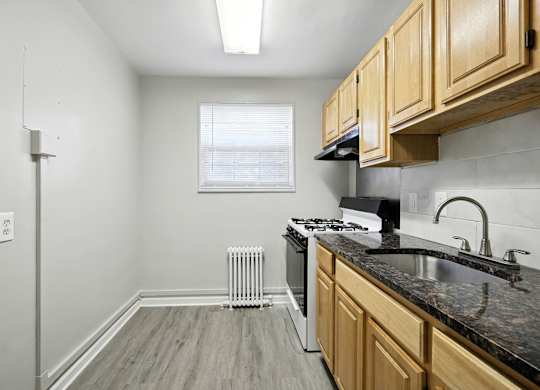 A kitchen with wooden cabinets and a black countertop at Huntwood Courts Apartments, Washington DC