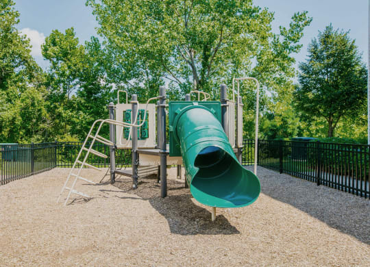 a large green slide in a park with trees in the background