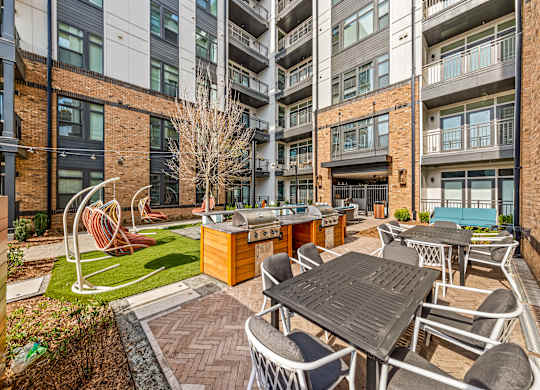 A patio with a table and chairs is surrounded by buildings at Hawkins Press Apartments, Charlotte, NC