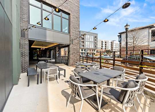 A patio with tables and chairs is surrounded by buildings at Hawkins Press Apartments, Charlotte
