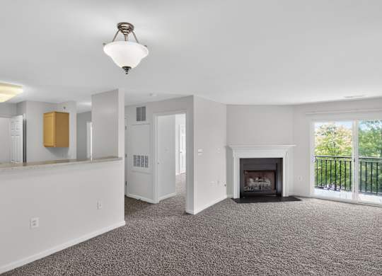 A large, empty living room with a fireplace and a balcony.