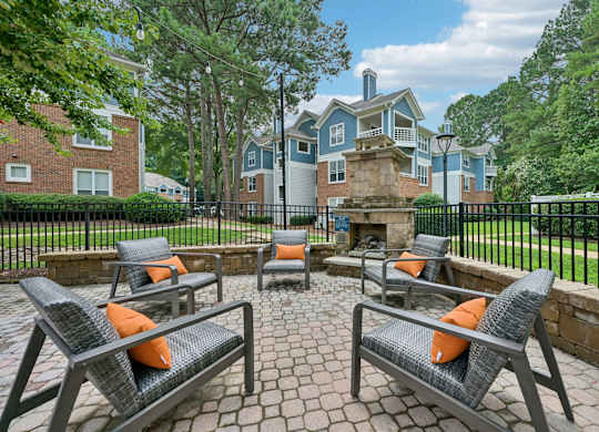 Four chairs are arranged around a fire pit on a brick patio.