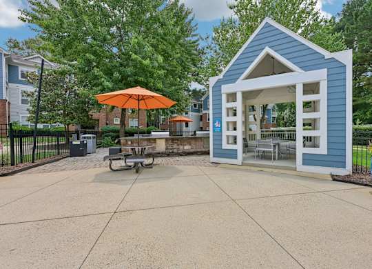 A small blue building with an orange umbrella sits in the middle of a paved area.