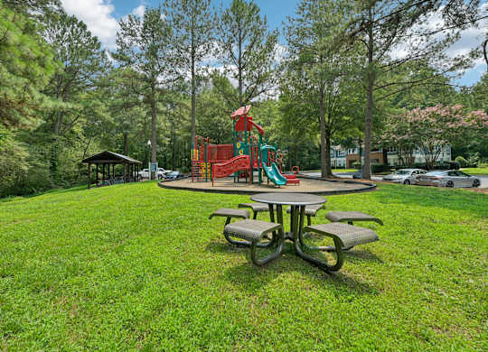 A playground with a red slide and a green slide is surrounded by trees.
